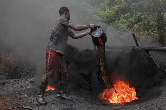 A man working at an illegal oil refinery site pours oil under a locally made burner to keep the fire going, near river Nun in Nigeria's oil state of Bayelsa November 27, 2012. Thousands of people in Nigeria engage in a practice known locally as “oil bunkering” – hacking into pipelines to steal crude then refining it or selling it abroad. The practice, which leaves oil spewing from pipelines for miles around, managed to lift around a fifth of Nigeria's two million barrel a day production last year according to the finance ministry. (Photo by Akintunde Akinleye/Reuters)