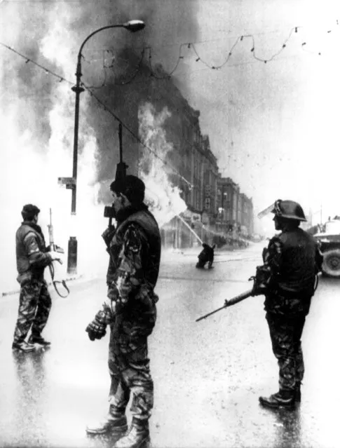 British soldiers stand guard as a department store goes up in flames in the center of Londonderry, Northern Ireland, on January 4, 1972. In center background, a fireman directs water into the blaze. The fire followed explosion of a bomb planted in the building by Irish Republican Army (IRA) terrorists. (Photo by AP Photo)