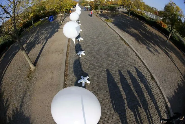 People cast shadows as they walk under stands with balloons placed along the former Berlin Wall location at Mauerpark, which will be used in the installation “Lichtgrenze” (Border of Light) in Berlin November 7, 2014. (Photo by Pawel Kopczynski/Reuters)