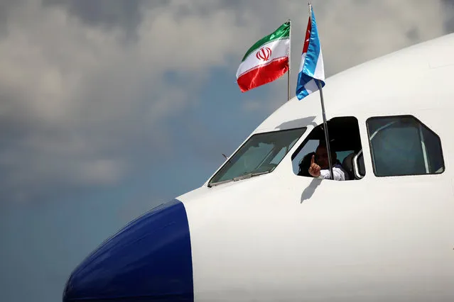 A pilot gestures as Iran and Cuba's flags hang at the cockpit of the airplane carrying Iran's President Hassan Rouhani upon his arrival at Jose Marti International Airport in Havana, Cuba September 19, 2016. (Photo by Alexandre Meneghini/Reuters)