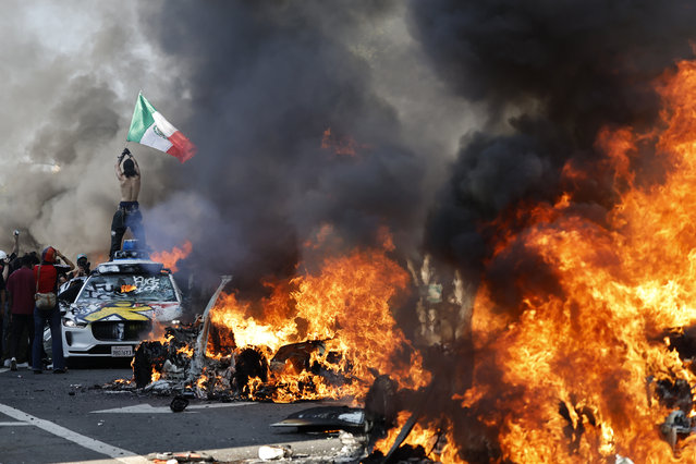 A protestor holds up a Mexican flag as burning cars line the street on June 08, 2025 in Los Angeles, California. Tensions in the city remain high after the Trump administration called in the National Guard against the wishes of city leaders following two days of clashes with police during a series of immigration raids. (Photo by Mario Tama/Getty Images)