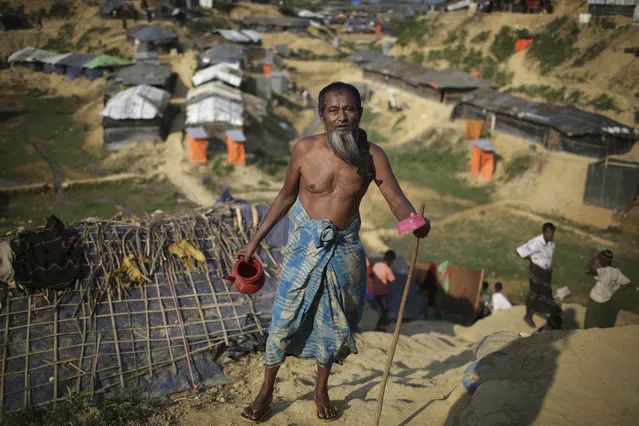 In this November 21, 2017, file photo, a Rohingya Muslim man carries his water pot and soap after a bath as he makes his way back to his tent, in Kutupalong refugee camp in Bangladesh. Since late August, more than 620,000 Rohingya have fled Myanmar's Rakhine state into neighboring Bangladesh, seeking safety from what the military described as “clearance operations”. The United Nations and others have said the military's actions appeared to be a campaign of “ethnic cleansing”, using acts of violence and intimidation and burning down homes to force the Rohingya to leave their communities. (Photo by Wong Maye-E/AP Photo)