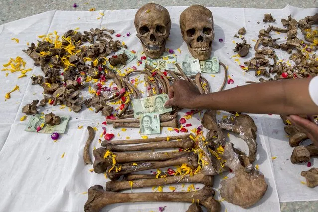 A volunteer puts a banknote on remains for luck during a mass exhumation at Poh Teck Tung Foundation Cemetery in Samut Sakhon province, Thailand November 3, 2015. (Photo by Athit Perawongmetha/Reuters)