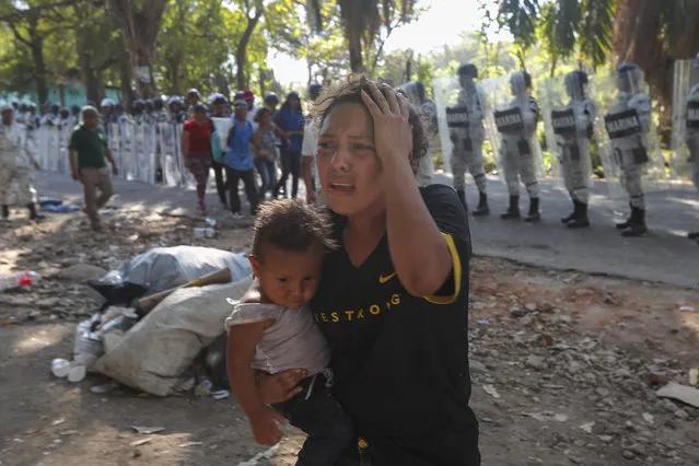 A female migrant carrying a child moves away from Mexican National Guards blocking the passage of a group of migrants near Tapachula, Mexico, Thursday, January 23, 2020. Hundreds of Central American migrants crossed the Suchiate River into Mexico from Guatemala Thursday after a days-long standoff with security forces. (Photo by Marco Ugarte/AP Photo)