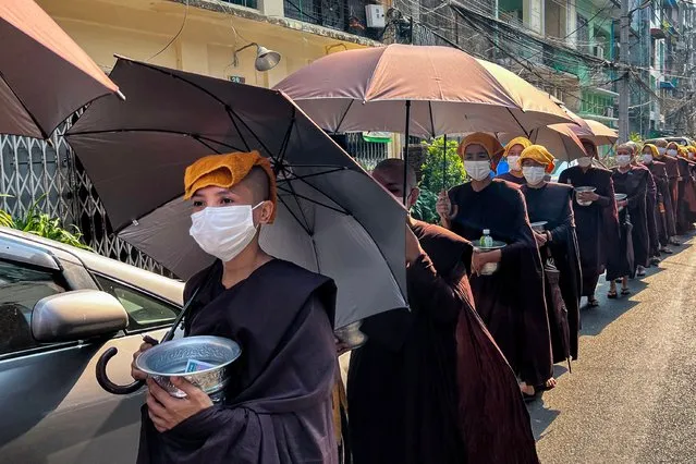 Buddhist nuns collect alms with their head covered with towels and under umbrellas to shelter from the sun during a heatwave in Yangon on April 24, 2023. Buddhist nuns collect alms shelter from the sun  as they during a heatwave in Yangon on April 24, 2023. (Photo by Sai Aung Main/AFP Photo)