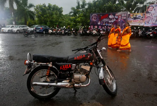Fans walk past a parked motorcycle decorated with the name of actor Rajinikanth's new movie “Kaala” outside a cinema hall in Mumbai, India, June 7, 2018. (Photo by Francis Mascarenhas/Reuters)