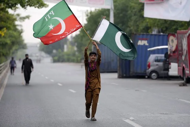 A supporter of Pakistan's former Prime Minister Imran Khan holds flags near his house, in Lahore, Pakistan, Wednesday, May 17, 2023. Police surrounded the home of Pakistan's former Prime Minister Khan on Wednesday, claiming he was sheltering dozens of people allegedly involved in violent protests over his recent detention. (Photo by K.M. Chaudary/AP Photo)
