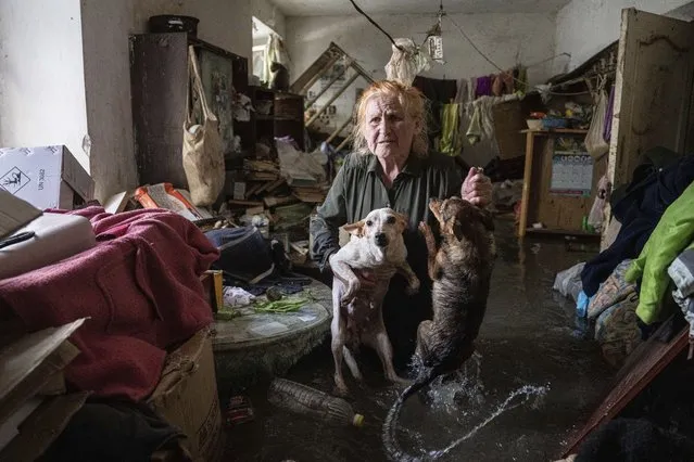Local resident Tetiana holds her pets, Tsatsa and Chunya, as she stands inside her house that was flooded after the Kakhovka dam blew up overnight, in Kherson, Ukraine, Tuesday, June 6, 2023. Ukraine on Tuesday accused Russian forces of blowing up a major dam and hydroelectric power station in a part of southern Ukraine that Russia controls, risking environmental disaster. (Photo by Evgeniy Maloletka/AP Photo)