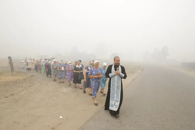 A priest and women take part in a religious procession, asking God for rains to prevent new wildfire outbursts, in the village of Kriusha, shrouded in heavy smog, some 250 km (155 miles) southeast of the capital in Ryazan region, August 7, 2010. Russian troops dug a 8-km (5-mile) long canal to keep fires caused by a record heatwave away from a nuclear arms site, local media said on Saturday as air pollution from the crisis rose to more than six times above normal. (Photo by Denis Sinyakov/Reuters)