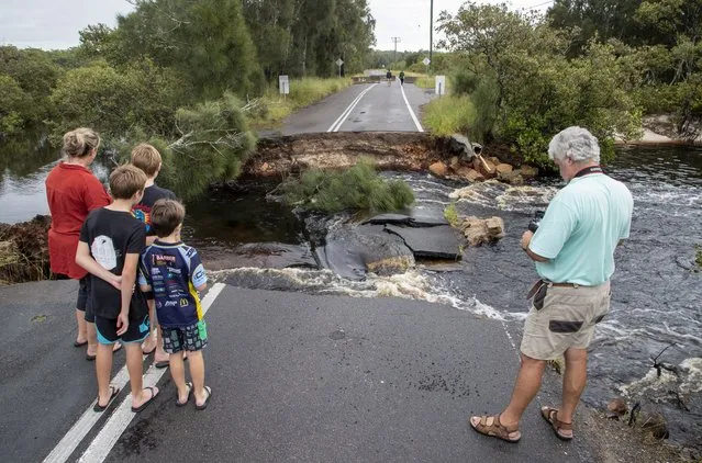 People stand at a washed out section of road at Port Stephens 200 kilometers (124 miles) north of Sydney, Australia, Saturday, March 20, 2021. People across New South Wales have been warned to expect intense rain and potentially life-threatening flooding, with Sydney predicted to be deluged with up to 200 millimeters of rain in one day. (Photo by Mark Baker/AP Photo)