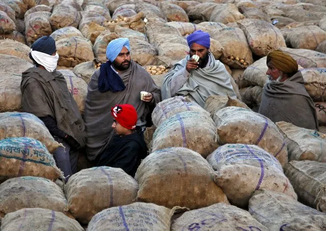 Farmers wearing shawls, drink tea amid sacks filled with potatoes at a wholesale vegetable market on a winter morning in Chandigarh, India, December 18, 2015. (Photo by Ajay Verma/Reuters)