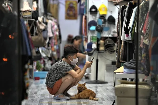 A vendor waits with her cat for customers at a store in Beijing, Thursday, July 27, 2023. (Photo by Ng Han Guan/AP Photo)