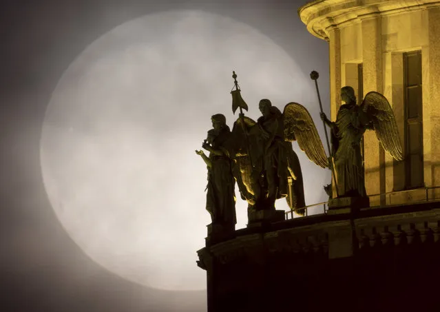 Sculptures of angels on the St. Isaac's Cathedral are silhouetted on the full moon rising in the clouds in St. Petersburg, Russia, Wednesday, May 26, 2021. (Photo by Dmitri Lovetsky/AP Photo)
