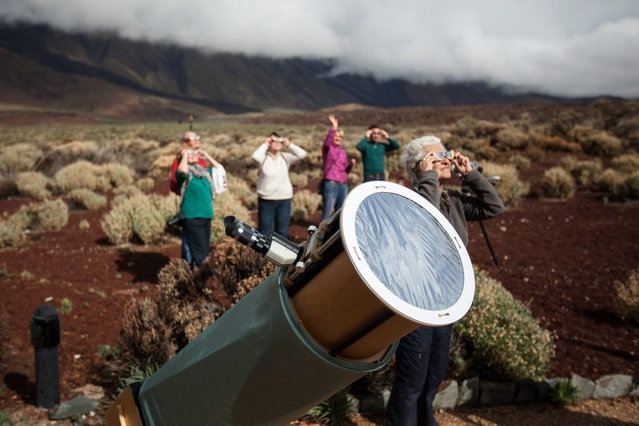 Next to a telescope, people look at the moon crossing in front of the sun during a partial solar eclipse in Santa Cruz de Tenerife in the Canary Islands, Spain, Sunday, Nov. 3, 2013. Clouds moving over the city allowed only brief views of the eclipse which in southern Europe was partial. The total eclipse was seen sweeping east across Africa. (Photo by Andres Gutierrez/AP Photo)