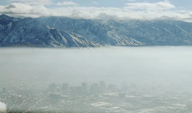 In this Wednesday, December 28, 2016 photo, the downtown skyline of Salt Lake City, Utah is shrouded in haze during an inversion. In the phenomenon, cold, stagnant air settles in the bowl-shaped mountain basins, trapping tailpipe and other emissions, creating a murky haze that engulfs the metro area. (Photo by Jeffrey D. Allred/The Deseret News via AP Photo)