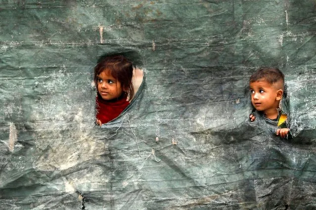 Children from an Afghan family look outside from a torn tent as they along with their family are returning home, after Pakistan gives the last warning to undocumented immigrants to leave, outside the United Nations High Commissioner for Refugees (UNHCR) repatriation centres in Azakhel town in Nowshera, Pakistan on November 1, 2023. (Photo by Fayaz Aziz/Reuters)
