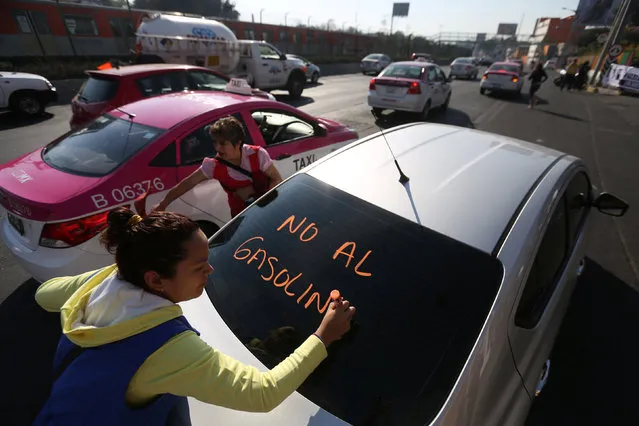 A protester writes on a car as she takes part during a demonstration at Tlalpan avenue against the rising prices of gasoline enforced by the Mexican government, in Mexico City, Mexico January 3, 2017. The words read “No more high prices of gasoline”. (Photo by Edgard Garrido/Reuters)