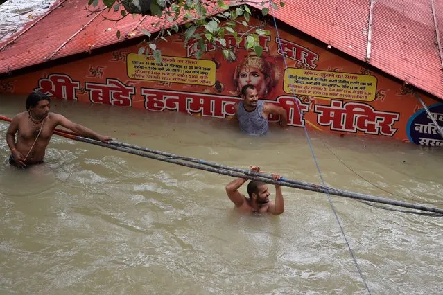 People take a dip outside a submerged Hanuman temple near as the water levels of the Ganges and Yamuna rivers rise in Allahabad on August 7, 2021. (Photo by Sanjay Kanojia/AFP Photo)