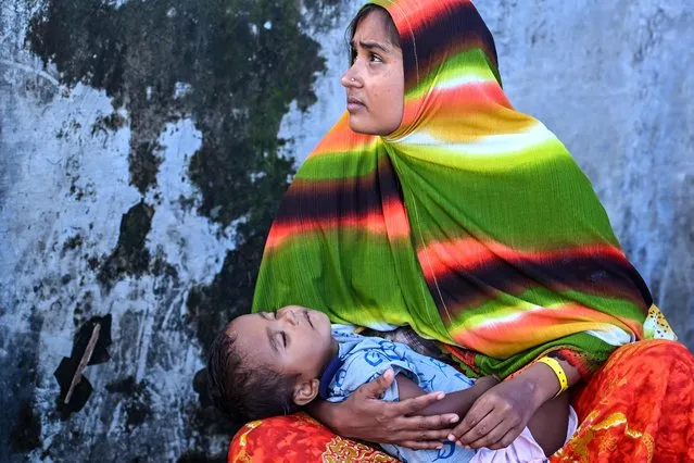 A Rohingya refugee woman looks on as she holds her child at a temporary camp, at a port in Sabang island, Indonesia's Aceh province on December 18, 2023. The mostly Muslim Rohingya were the target of a 2017 crackdown by Myanmar's military that is the subject of a UN genocide probe. Around a million have fled to Bangladesh, and from there thousands risk their lives each year on long and expensive sea journeys to reach Malaysia or Indonesia. (Photo by Chaideer Mahyuddin/AFP Photo)