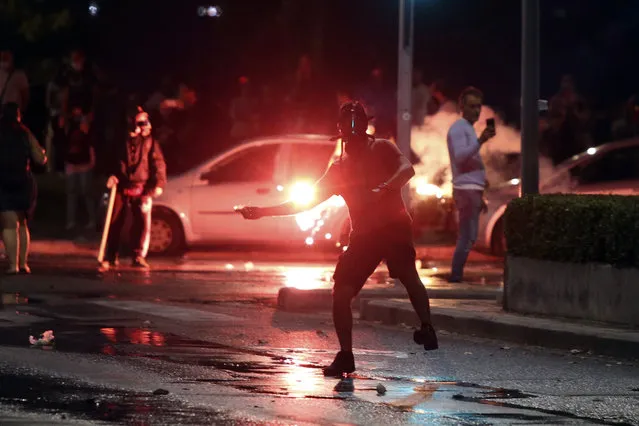 An anti-vaccine protester throws a flare during a rally, at the northern city of Thessaloniki, Greece, Saturday, September 11, 2021. While Greece's Prime Minister, Konstantinos Mitsotakis was touting the achievements of his government despite the pandemic emergency, some 3,500 vaccination deniers clashed with riot police near the venue. (Photo by Giannis Papanikos/AP Photo)