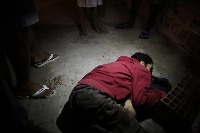 Nelson Eduardo Conclaves lies in a pool of blood as a neighbor stands over him in Vitoria, Espirito Santo state, Brazil, Thursday, February 9, 2017. According to his mother Erlita Pereira Goncalves, her 30-year-old son was shot dead by attackers who broke into their home and killed him in front of her. (Photo by Diego Herculano/AP Photo)