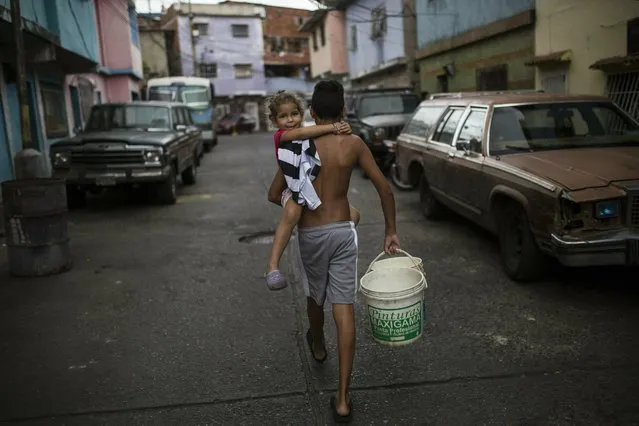 Jose Assuage, 13, carries his cousin Naomi, 4, as he goes in search of water in the 23 de Enero neighborhood, in Caracas, Venezuela, Friday, May 3, 2019. (Photo by Rodrigo Abd/AP Photo)