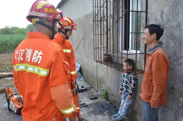 The father of a boy smiles as firemen rescue the boy whose head is stuck between protective bars outside a window in Wuhan, Hubei Province, China, in this April 11, 2016 picture. (Photo by Reuters/Stringer)