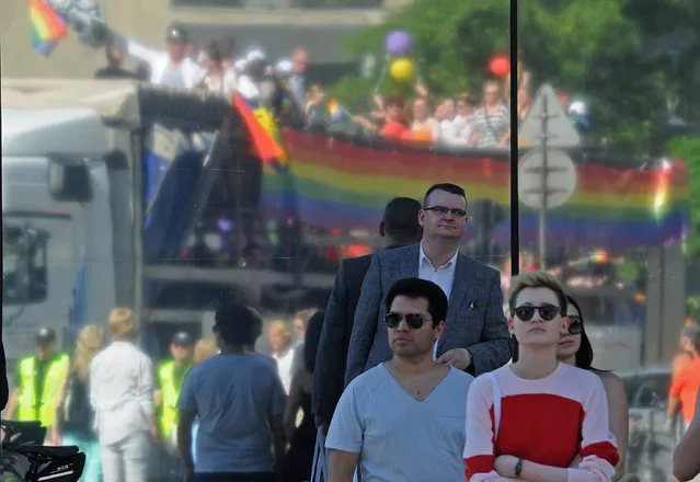 Passersby watch a gay pride parade, seen reflected in a shop window, in Warsaw, Poland, Saturday, June 13, 2015. Gay rights activists hold their 15th yearly "Equality Parade" as Poland slowly grows more accepting of gays and lesbians, but where gay marriage, and even legal partnerships, still appear to be a far-off dream. This year's parade comes amid a right-wing political shift, a possible setback for the LGBT community. (AP Photo/Alik Keplicz)