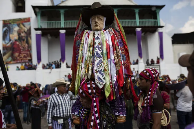 In this Wednesday, April 12, 2017 photo, Maya priest Juan Tacaxoy carries a wooden statue of folk saint Maximon in a Holy Week procession as he arrives to the town hall in Santiago Atitlan, Guatemala. Venerated mostly by Mayan indigenous communities in the highlands of Western Guatemala, Maximon is a mix of wise man, healer and avenger, representing both dark and light. (Photo by Moises Castillo/AP Photo)
