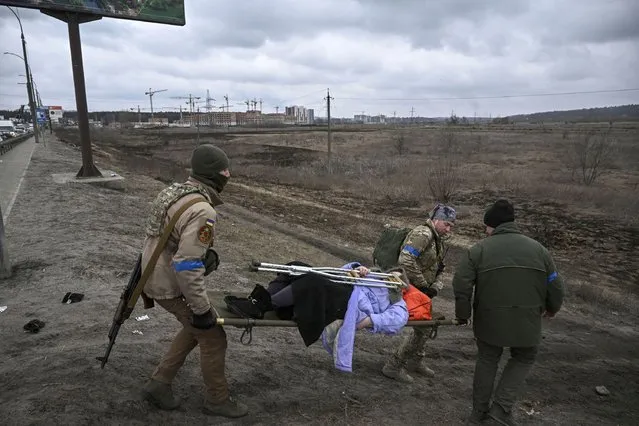 Ukrainian servicemen evacuate an elderly woman on a stretcher from the city of Irpin on March 13, 2022. Russian forces advance ever closer to the capital from the north, west and northeast. Russian strikes also destroy an airport in the town of Vasylkiv, south of Kyiv. A US journalist was shot dead and another wounded in Irpin, a frontline northwest suburb of Kyiv, medics and witnesses told AFP. (Photo by Aris Messinis/AFP Photo)