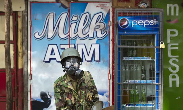 A Kenyan policeman wears a gas mask as he stands in from of a milk dispenser at a kiosk, during running battles between police firing tear gas and protesters throwing rocks, in the Kibera slum of Nairobi, Kenya Monday, May 23, 2016. (Photo by Ben Curtis/AP Photo)