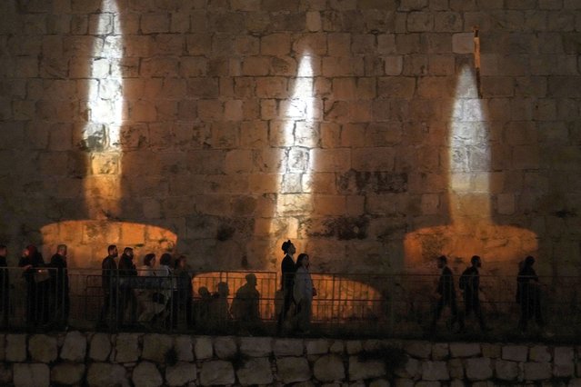 People walk by an image of memorial candles, projected on the walls of Jerusalem's Old City on the eve of annual Holocaust Remembrance Day, Monday, April 17, 2023. Israel holds the day of remembrance each year to remember the six million Jewish victims of the Nazi genocide during World War II. (Photo by Mahmoud Illean/AP Photo)