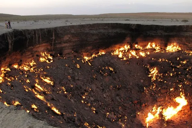 A picture taken on May 3, 2014, shows people visiting “The Gateway to Hell”, a huge burning gas crater in the heart of Turkmenistan's Karakum desert. The fiery pit was the result of a simple miscalculation by Soviet scientists in 1971 after their boring equipment suddenly drilled through into an underground cavern and a deep sinkhole formed. Fearing that the crater would emit poisonous gases, the scientists took the decision to set it alight, thinking that the gas would burn out quickly and this would cause the flames to go out. (Photo by Igor Sasin/AFP Photo)