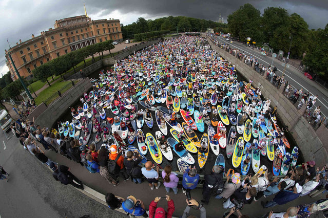 People steer their stand-up paddle (SUP) boards along Moyka River during annual costumed 'Fontanka' SUP-boards festival in St. Petersburg, Russia, Saturday, August 3, 2024. (Photo by Dmitri Lovetsky/AP Photo)