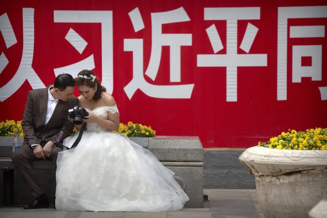 In this May 19, 2018, file photo a couple in wedding dress look at photos on the back of a camera near a propaganda slogan with the name of Chinese President Xi Jinping in Beijing. Chinese leaders have long been sensitive about their communist country’s international image. Now, they are battling back, investing in diplomacy and a courtship of hearts and minds, just as the United States digs in on the Trump administration’s “America First” mindset. (Photo by Mark Schiefelbein/AP Photo/File)