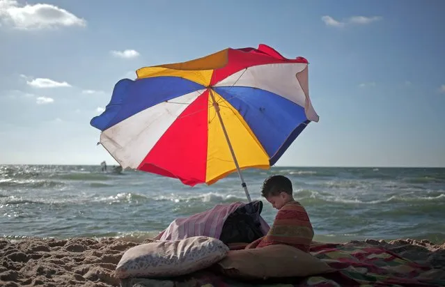In this Monday, June 23, 2014 photo, a Palestinian boy sits under an umbrella as he and others enjoy a summer day at the beach of Gaza City. (Photo by Khalil Hamra/AP Photo)