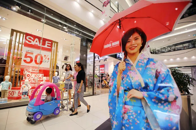 Shoppers walk past sale signs in a store window at the Aeon Co. mall in the Long Bien district of Hanoi, Vietnam, on Thursday, July 21, 2016. With a young population, an expanding middle class and one of Southeast Asia's fastest-growing economies, Vietnam is an alluring market for Aeon. The reason: China is slowing and growth is flat-lining at home. (Photo by Luong Thai Linh/Bloomberg)