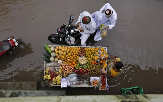 People buy fruits from a street hawker on a waterlogged road after heavy rain in the western Indian city of Ahmedabad July 18, 2014. The monsoon rains were 15 percent below average in the past week, against 41 percent below average rainfall in the previous week, the weather office data showed. On Thursday, the annual rains covered the entire country two days later than schedule. (Photo by Amit Dave/Reuters)