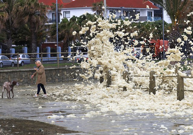 A woman with her dog avoids sea foam at Three Anchor Bay during a cold front in Cape Town, South Africa, on August 28, 2024. (Photo by Esa Alexander/Reuters)