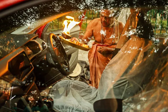 In this picture taken on August 1, 2022, a priest performs a ritual on a newly purchased car to seek blessings from the deities for safety outside a temple in Bangalore. (Photo by Sebastien Berger/AFP Photo)
