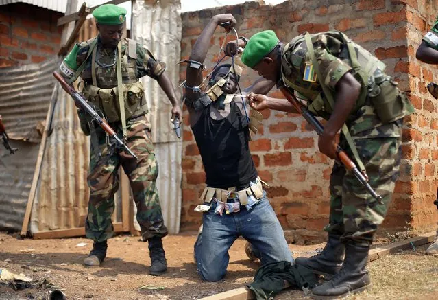 In this Wednesday January 22, 2014 photo, Rwandan African Union peacekeepers remove the lucky charms from a suspected Anti-Balaka Christian man who was found with a rifle and a grenade following looting in the Muslim market of the PK13 district of Bangui, Central African Republic. A sweeping United Nations report has identified hundreds of human rights violations in Central African Republic that may amount to war crimes. The Tuesday may 30, 2017, report comes amid growing fears that the country terrorized by multiple armed groups is once again slipping into the sectarian bloodshed that left thousands dead between late 2013 and 2015. (Photo by Jerome Delay/AP Photo)
