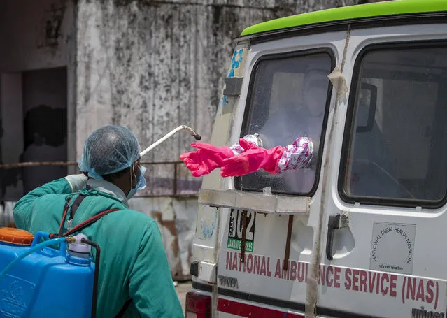 A health worker sprays disinfectant on the gloves of a doctor sitting inside a van to collect samples from people to be tested for the coronavirus in Dharmsala, India, Saturday, May 9, 2020. India relaxed some coronavirus lockdown restrictions on Monday even as the pace of infection picked up and reopenings drew crowds of people. (Photo by Ashwini Bhatia/AP Photo)
