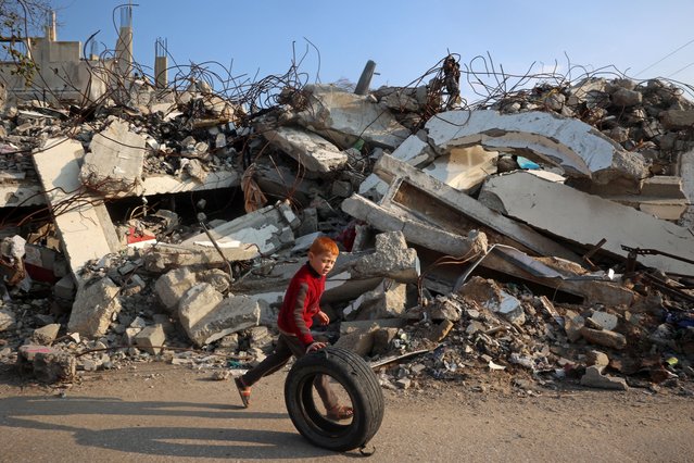 A boy plays with a rubber tyre next to the rubble of buildings destroyed in Israeli airstrikes near the Nuseirat refugee camp in the central Gaza Strip on January 11, 2025, as the war between Israel and Hamas militants continues. (Photo by Eyad Baba/AFP Photo)