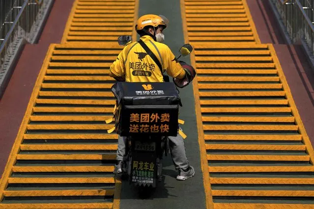 A food delivery rider wearing a face mask pushes his electric bike up to a pedestrian bridge in Beijing, Monday, September 26, 2022. (Photo by Andy Wong/AP Photo)