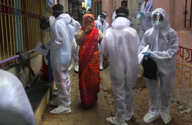 A woman covers her face as she walks past health workers arriving to administer a free medical checkup in a slum in Mumbai, India, Sunday, June 28, 2020. India is the fourth hardest-hit country by the COVID-19 pandemic in the world after the U.S., Russia and Brazil. (Photo by Rafiq Maqbool/AP Photo)