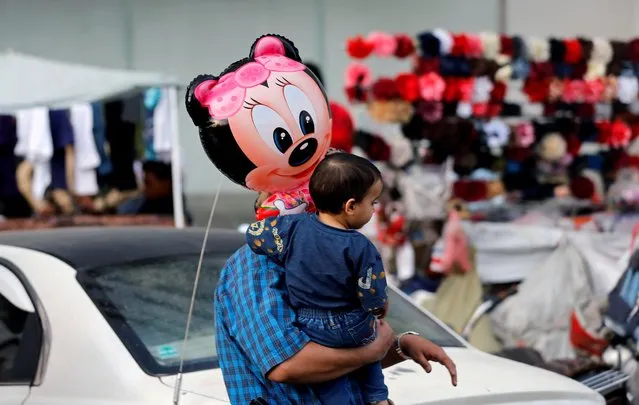 A man carries his son who holds a balloon outside a shopping mall ahead of Eid al-Fitr holiday, amid concerns of the spread of the coronavirus disease (COVID-19), in Sanaa, Yemen on May 17, 2020. (Photo by Khaled Abdullah/Reuters)
