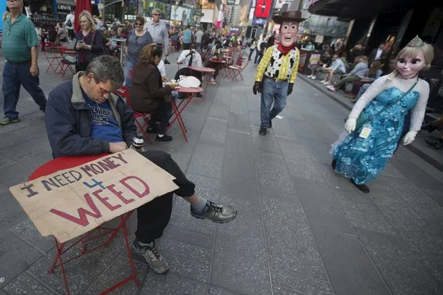 A man sleeps at a table with his "I need money 4 weed" sign as costumed characters walk past in Times Square in the Manhattan borough of New York October 8, 2015. (Photo by Carlo Allegri/Reuters)