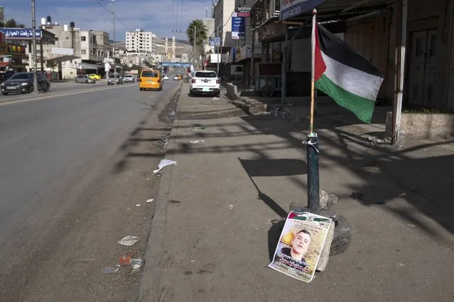 A Palestinian flag and a poster showing Ammar Adili, 22, who was shot and killed by an Israeli border police officer on Friday, mark the location of the incident, on the main thoroughfare where shops are closed in a general strike, in the West Bank town of Hawara, south of Nablus, Saturday, December 3, 2022. Palestinians pushed back Saturday against Israeli police claims that Ammar Adili had attacked Israelis, including a border policeman, in the area and that he was shot in self-defense. They said the officer killed Adili without cause, and that Palestinian medics were kept from trying to save him as he lay gravely wounded on the side of a busy throughfare in the occupied West Bank town of Hawara. (Photo by Nasser Nasser/AP Photo)