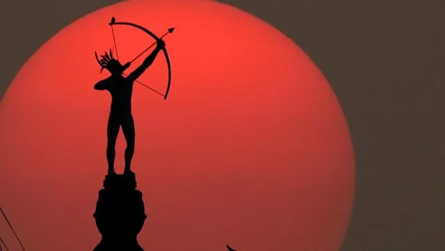 The bronze sculpture of Ad Astra, a Kansa Indian, perched atop the Kansas Statehouse dome, is silhouetted against the setting sun, Thursday, September 17, 2020, in Topeka, Kan. Sunsets across much of the country have been more vibrant than usual as smoke from western wildfires drifts across the nation. (Photo by Charlie Riedel/AP Photo)