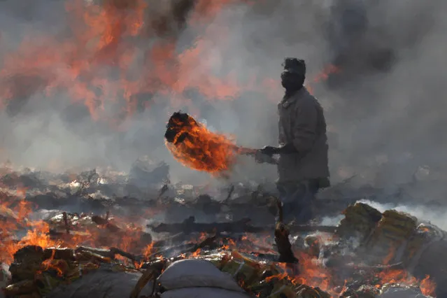 Pakistani Customs employee with fire torch stands amid burning piles of confiscated contraband and narcotics destroyed during a campaign marking International Customs Day in Karachi, Pakistan January 26, 2018. (Photo by Akhtar Soomro/Reuters)